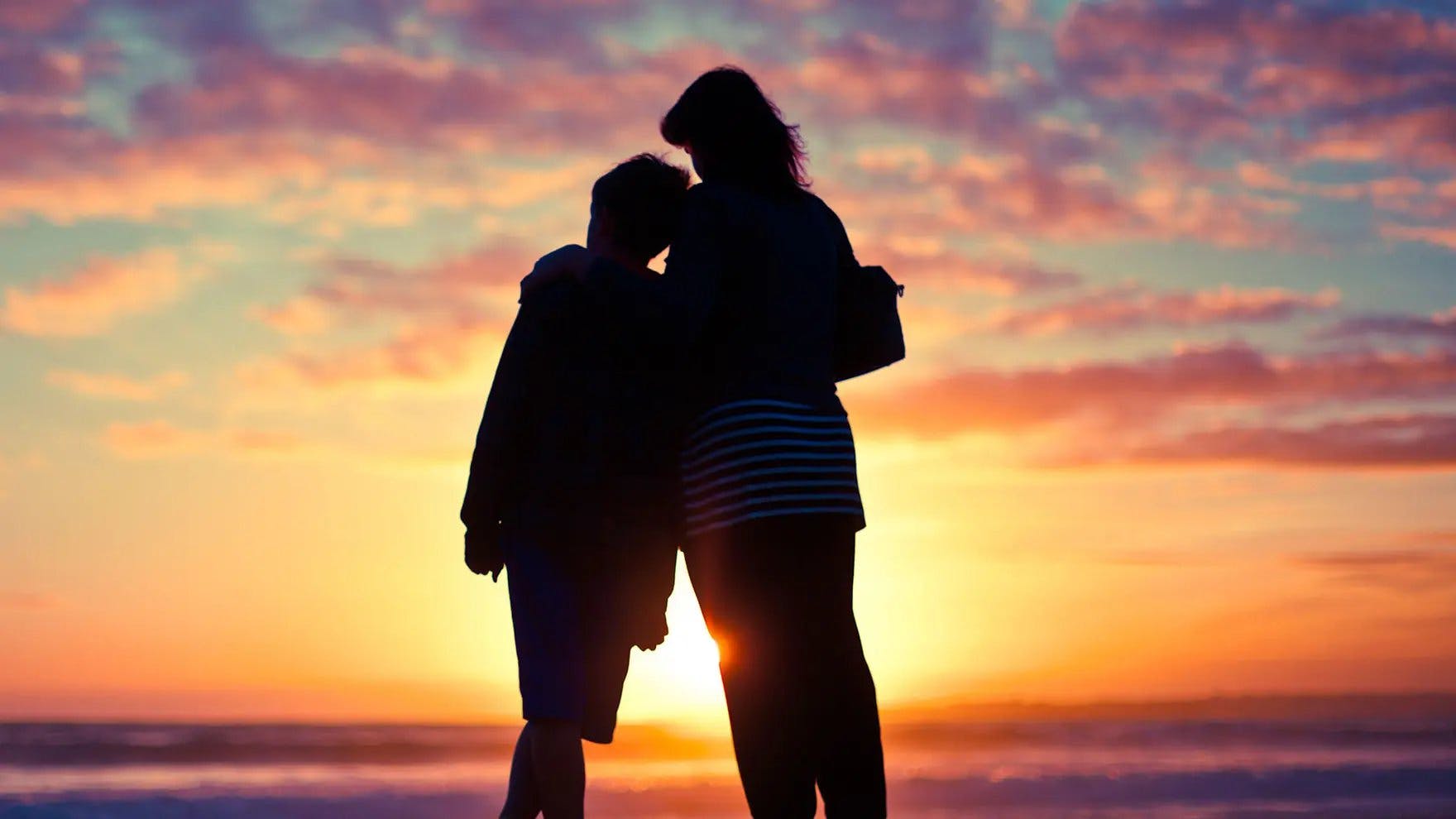 Two people standing on beach in front of sunset